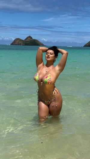 Woman in colorful bikini posing in turquoise ocean water near hills.