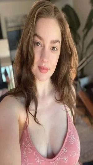 Curvy brunette in pink camisole, indoor selfie.