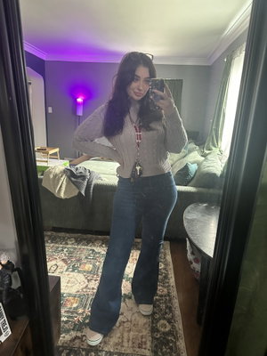 Curvy woman taking mirror selfie in bedroom wearing sweater and jeans.