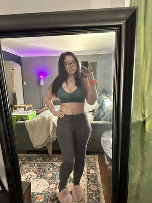 Woman with glasses in sports bra and leggings taking mirror selfie.
