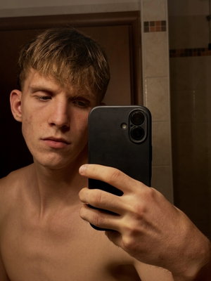 Young man taking shirtless selfie in bathroom.