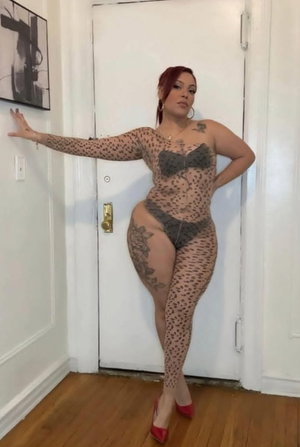 Curvy redhead woman in sheer polka-dot outfit posing indoors.