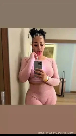 Woman in pink crop top and leggings takes mirror selfie, sticking out tongue.
