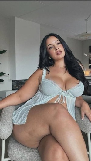 Curvy woman with long dark hair wearing light blue lingerie indoors.