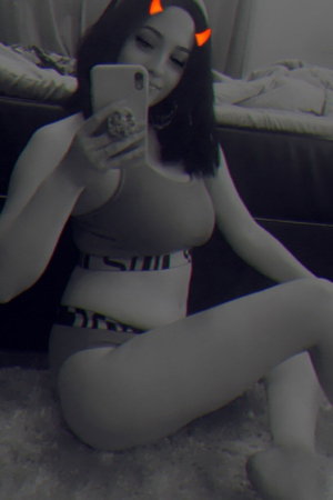 Dark-haired woman in crop top and panties taking bedroom selfie.