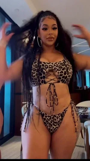 Woman in leopard print bikini posing indoors, long dark hair, large hoop earrings.