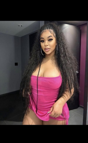 Woman with long curly hair in pink dress posing indoors.