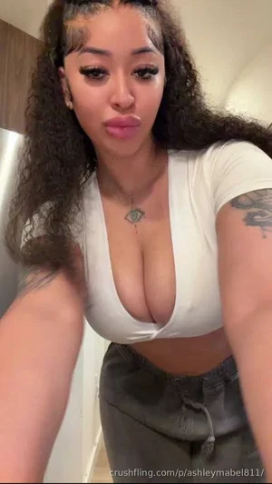 Woman with curly hair in white crop top and dark pants, posing indoors.