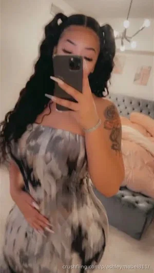 Woman with long dark hair in pigtails, wearing a patterned strapless dress, taking mirror selfie in