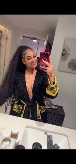 Woman with long dark hair in black and yellow robe taking mirror selfie in bathroom.