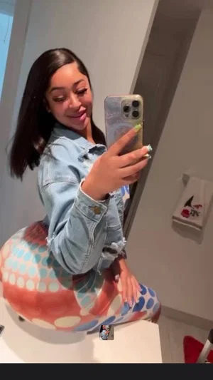 Woman in denim jacket and colorful polka-dot pants taking mirror selfie in bathroom.
