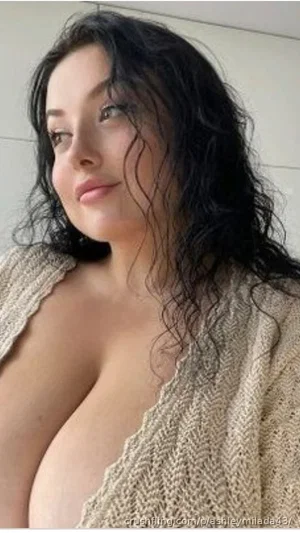 Woman with dark curly hair wearing an open knit cardigan, showing bare shoulders and chest.