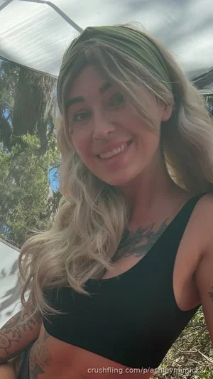 Woman with blonde hair and tattoos wearing black crop top outdoors.
