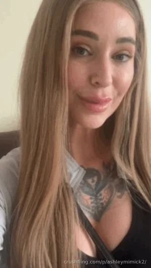 Woman with long blonde hair, chest tattoo, wearing black top, indoor setting.