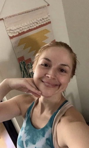 Woman in teal tank top smiling, indoor setting with woven wall hanging.