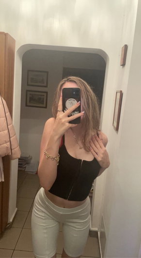 Woman in black crop top and white shorts taking mirror selfie in hallway.