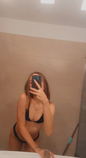 Woman in black bikini taking mirror selfie in bathroom.