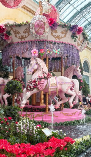 Pink carousel with floral horses in indoor garden setting.