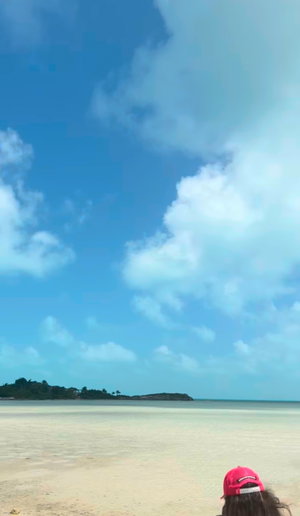 Person in red cap at beach, back view, clear sky and water.