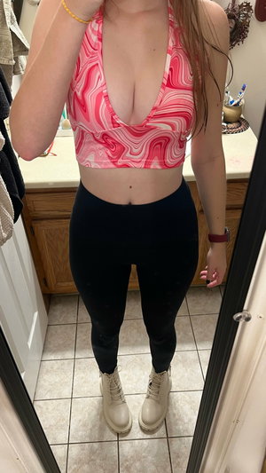 Curvy woman in pink crop top and black leggings in bathroom.