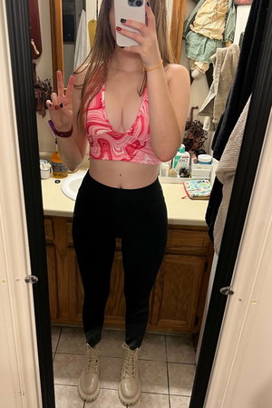 Woman in pink crop top and black leggings mirror selfie in bathroom.