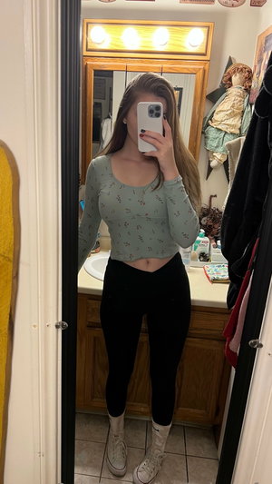 Woman taking mirror selfie in bathroom wearing crop top and leggings.