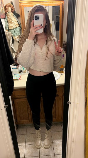 Woman taking mirror selfie in bathroom wearing cropped sweater.