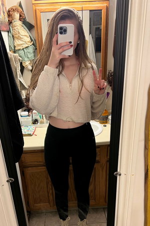 Brunette woman in crop top taking mirror selfie in bathroom.