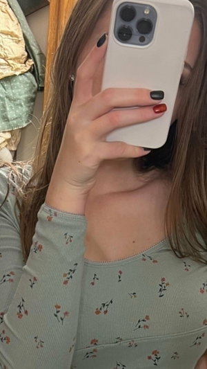 Woman with long brown hair in floral top taking mirror selfie indoors.