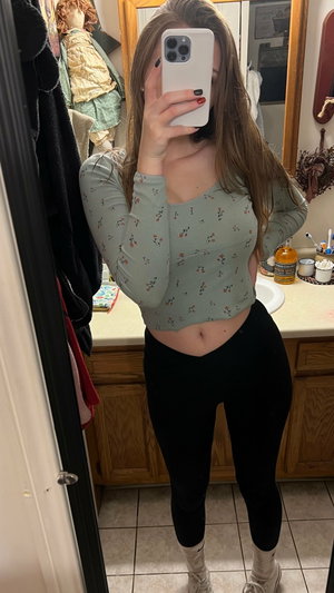Woman in floral top and black leggings taking bathroom mirror selfie.