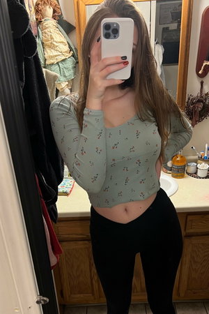 Woman taking mirror selfie in bathroom wearing floral crop top.