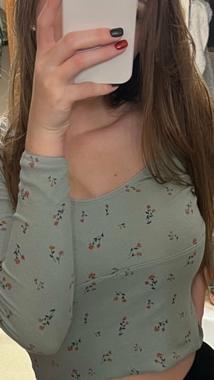 Woman with long brown hair in floral top holding phone to face, indoor setting.