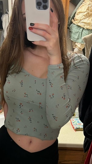 Woman in floral crop top and black pants taking mirror selfie in bedroom.