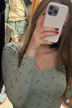 Woman in floral long-sleeve top taking mirror selfie, hair covering face partially.