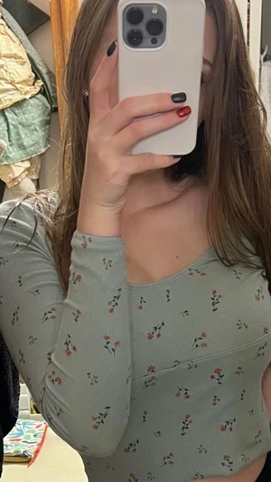 Woman in floral long-sleeve top taking mirror selfie, indoor setting.