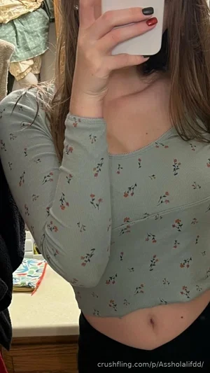 Woman in floral long-sleeve crop top, holding phone, indoor setting.
