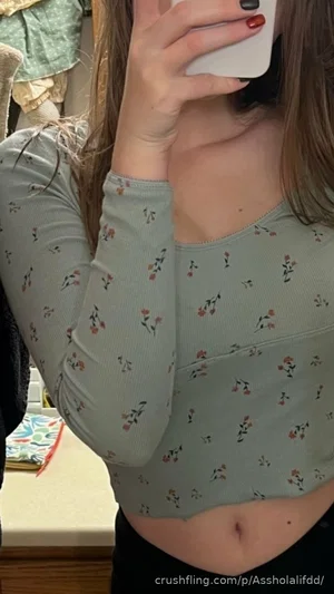 Woman in floral long-sleeve crop top, holding phone, indoor setting.