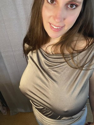 Woman with long brown hair in shiny top taking selfie indoors.