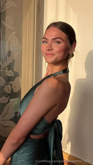 Woman in a dark green halter dress posing indoors near a floral-patterned window.