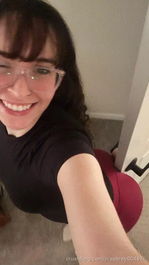 Woman with dark hair and glasses in black top, smiling in indoor setting.