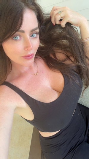 Woman with long brown hair in black top taking indoor selfie.