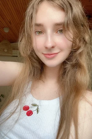 Blonde woman in white tank top takes indoor selfie.