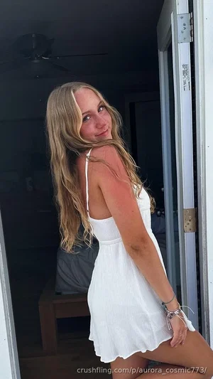 Blonde woman in white dress posing in doorway, indoor setting.