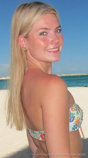 Blonde woman in floral bikini on beach, smiling over shoulder.