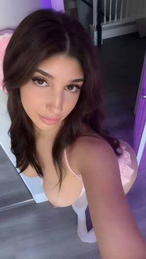 Dark-haired woman in pink lingerie taking a bedroom selfie.
