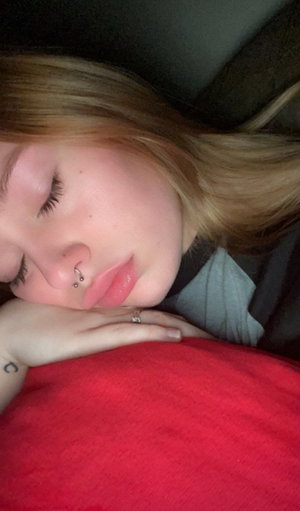 Woman with blonde hair sleeping, wearing gray top, resting on red blanket.
