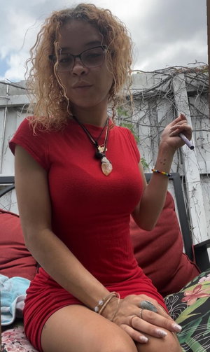Curly haired woman in red dress sitting outdoors.