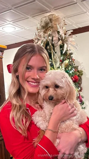 Woman in red top holding small dog in front of decorated Christmas tree indoors.