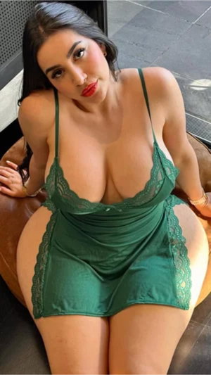 Woman in green lace lingerie posing on a brown leather chair indoors.