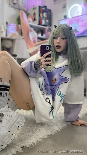 Woman with green hair and tattoos in oversized hoodie, taking mirror selfie in room with neon